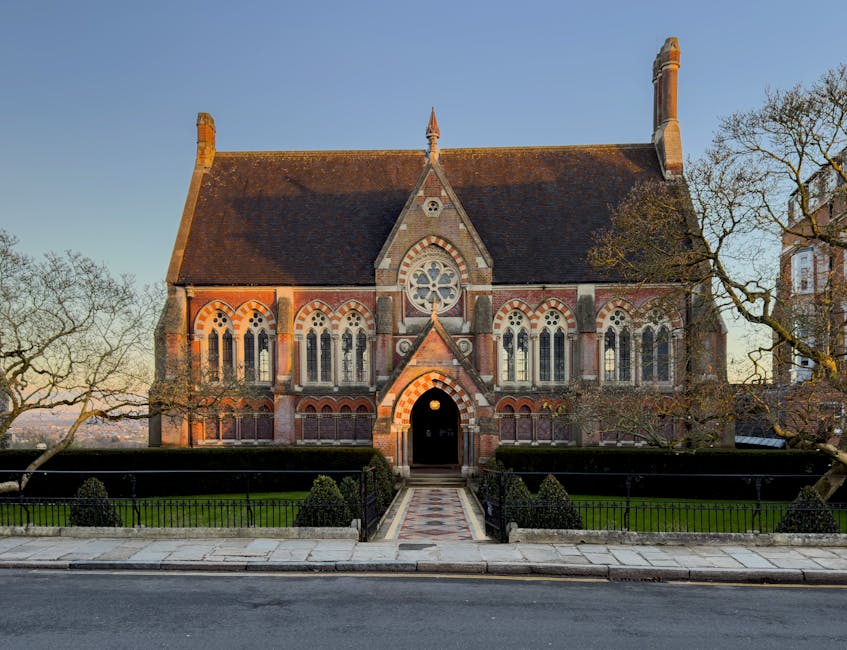 The brick façade of a historic Victorian-style home located on Church Hill features decorative stepped gables and tall sash windows. The property is enclosed by a black wrought iron fence atop a low b